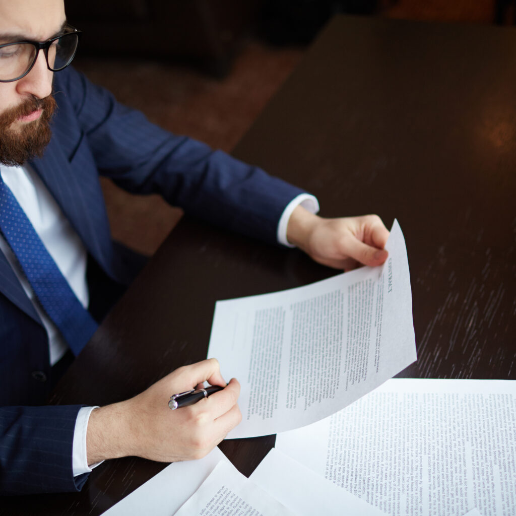 Image of serious businessman signing contract at workplace