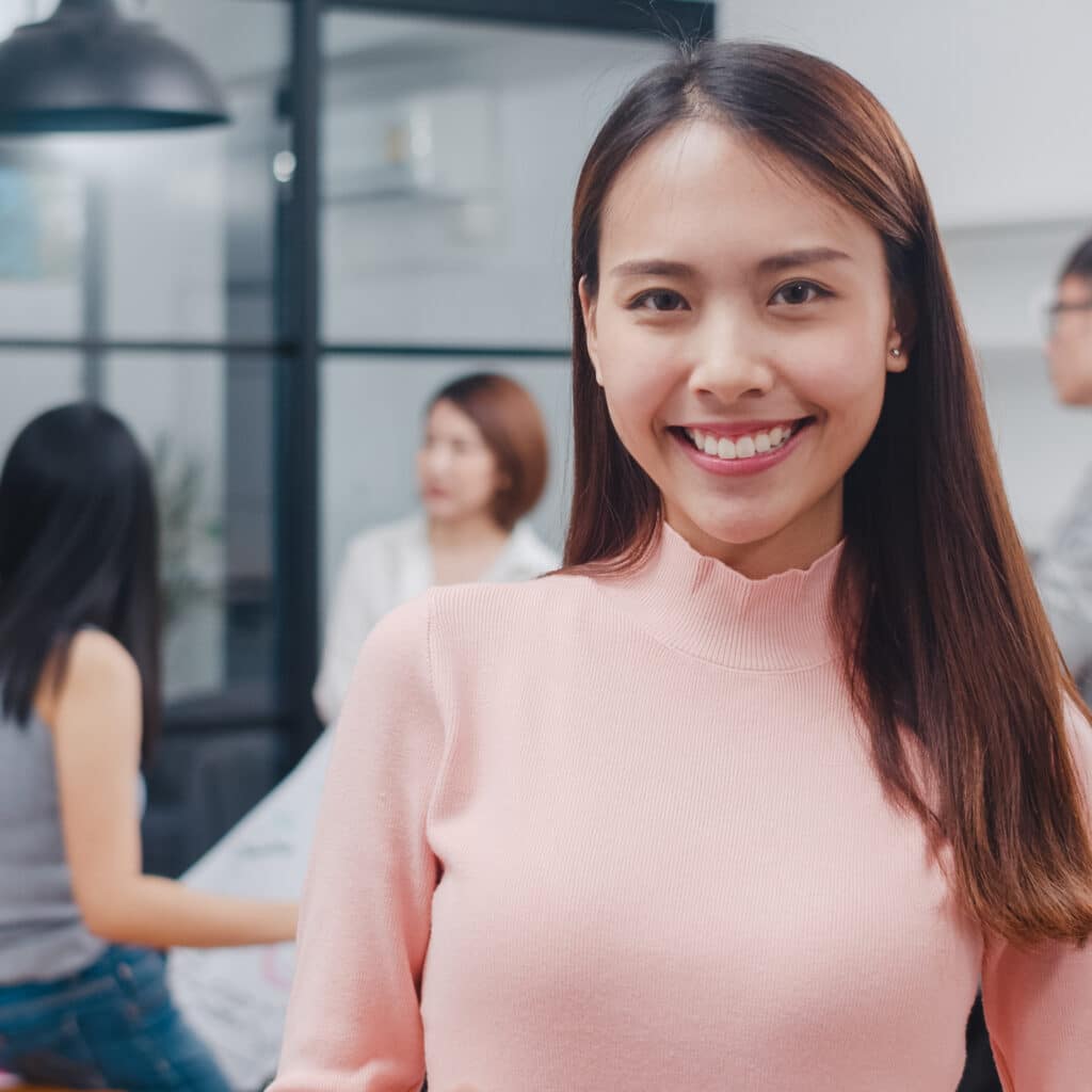 Portrait of successful beautiful executive businesswoman smart casual wear looking at camera and smiling, happy in modern office workplace. Young Asia lady standing relax in contemporary meeting room.